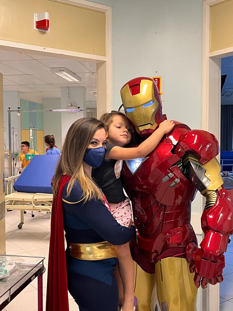 Menina abraçando o Coração de Aço no colo de uma voluntária