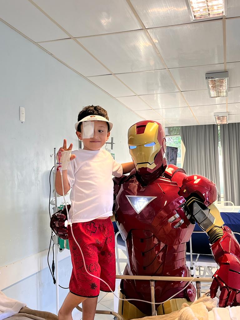 Menino fazendo sinal de paz ao lado do Coração de Aço no quarto do hospital